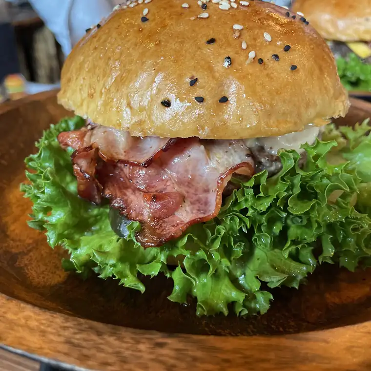 Burger z bekonem, sałatą i serem na drewnianym talerzu
